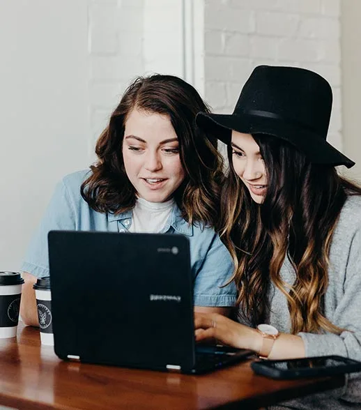 Zwei Mädchen verschriftlichen ein Interview an schwarzem Laptop